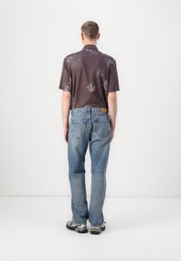 Chemise à manches courtes à motifs floraux foncés associée à un jean droit bleu clair, avec poches arrière et un patch en cuir à la taille.