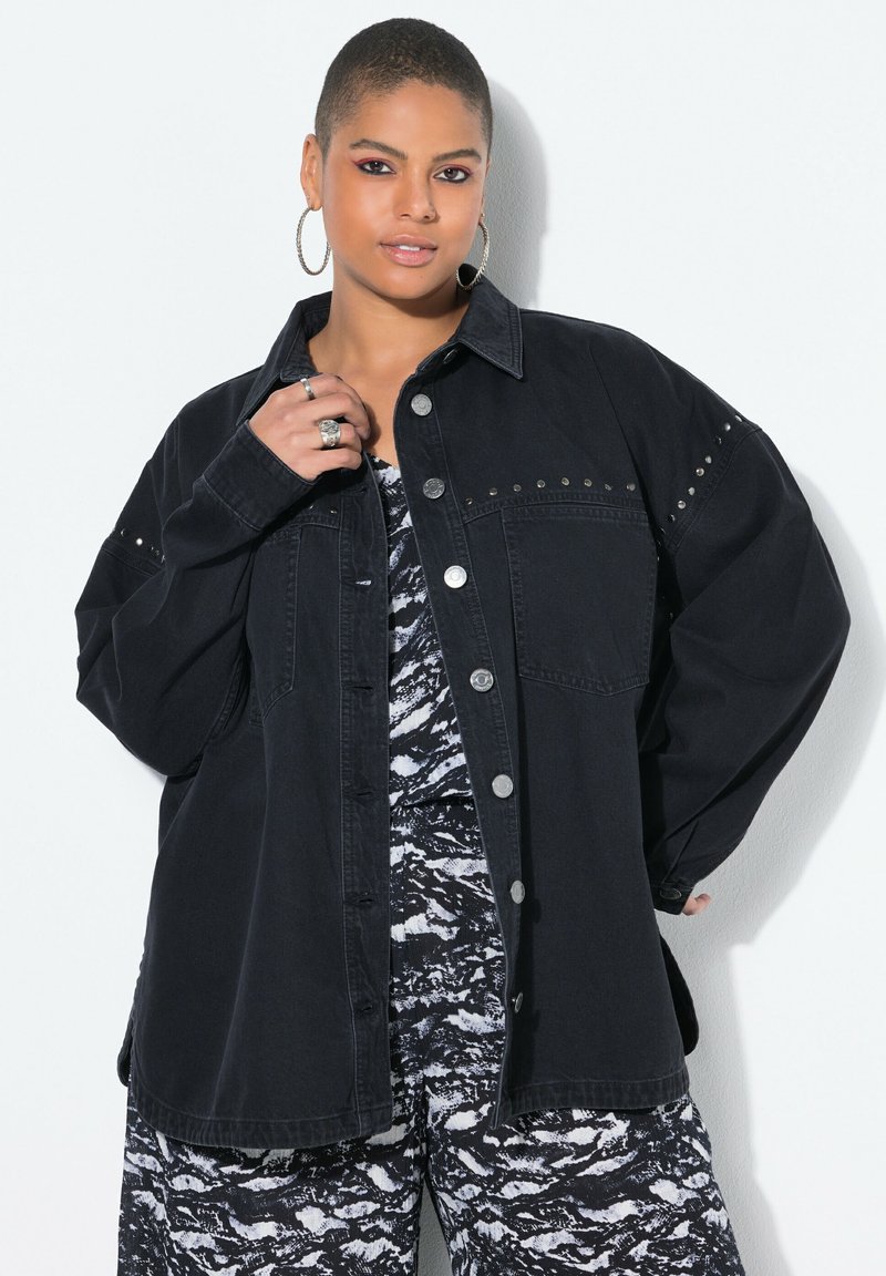 Giubbotto in denim nero con chiusura a bottoni, vestibilità oversize e applicazioni di borchie sulle spalle. Tessuto testurizzato con ampie tasche.
