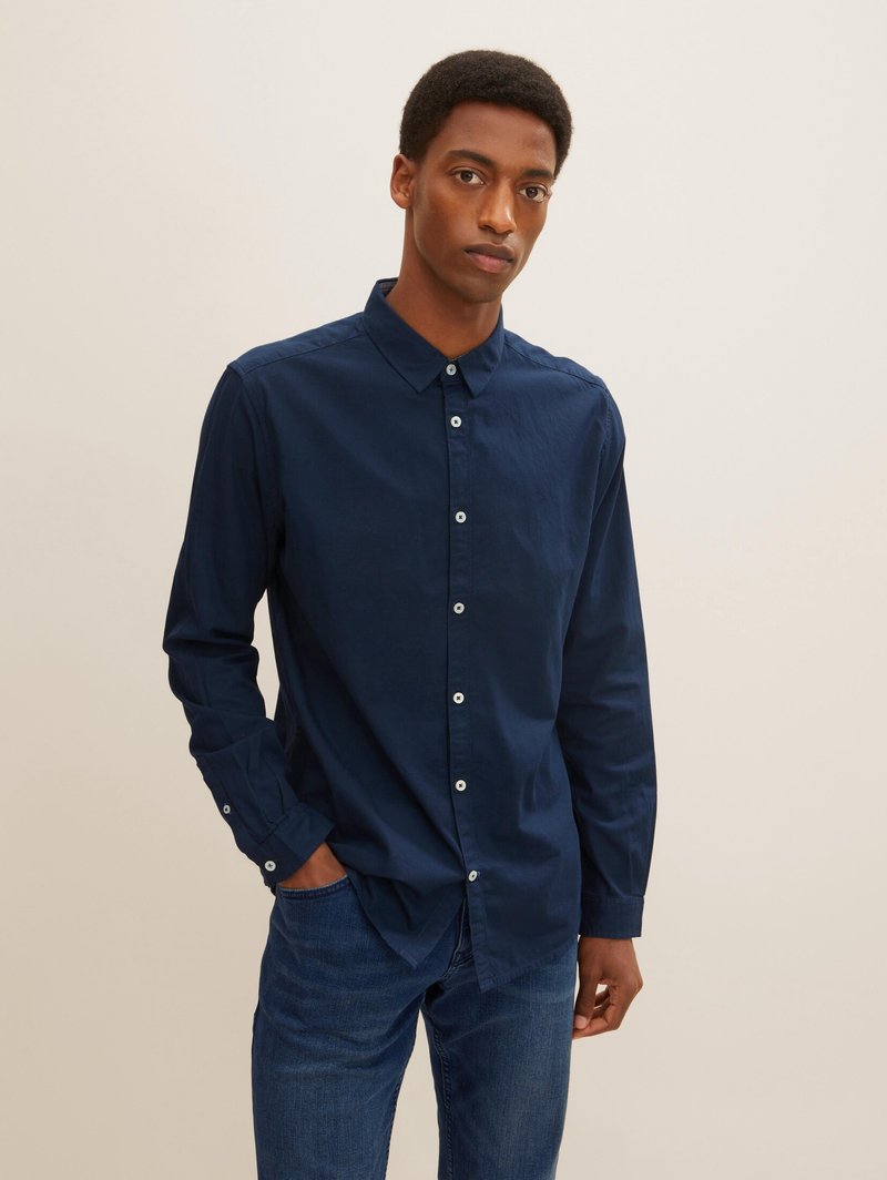 Navyblaues Hemd mit Knöpfen aus Baumwolle, mit Kragen, langen Ärmeln und kontrastierenden weißen Knöpfen. Getragen mit dunklen Jeans.