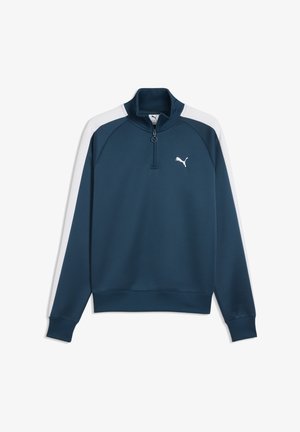 Marineblå pullover med hvide skulderstriber, kvart lynlås, ribbet krave, manchetter, kant og lille hvid Puma-logo på venstre bryst.