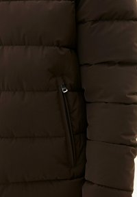 Bruine pufferjack met quilted secties, voorzien van een zijzak met ritssluiting en een gladde, matte textuur.