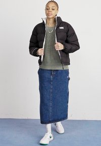 Black puffer jacket with gray lining, green knit sweater, and a long blue denim skirt. White sneakers feature green accents. Plain background.