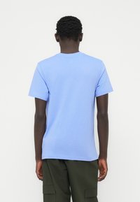 Ανοιχτό μπλε βαμβακερό μπλουζάκι με κοντά μανίκια, στρογγυλή λαιμόκοψη και απαλή υφή, ορατό από πίσω. Χωρίς ορατά σχέδια ή διακοσμητικά στοιχεία.