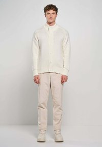 Cardigan lavorato a maglia crema con polsini e orlo a coste, con bottoni frontali. Abbinato a pantaloni beige chiaro e sneakers bianche.