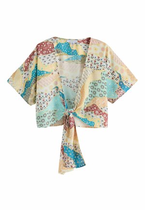 Žena s veľkými jantárovými slnečnými okuliarmi a farebným patchwork krátkym rukávom zauzleným v páse so zodpovedajúcimi nohavicami s vysokým pásom.