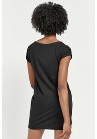 Musta lyhythihainen mekko pyöreällä pääntiellä, istuvalla siluetilla ja sileällä pinnalla, joka esittelee minimalistista muotoilua ja ulottuu reisien puoliväliin.