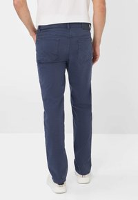 Dunkelblaue Hose aus Baumwolle. Verfügt über einen klassischen Schnitt, zwei hintere Taschen mit Stitching-Details und ein Etikett am Bund.