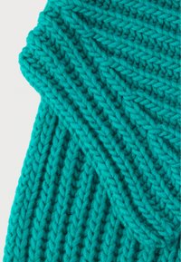 Pletená textília v žiarivej tyrkysovej farbe, s textúrovaným diagonálnym rebrovaným vzorom a mäkkou, hrubou priadzou. Bez viditeľných kovových prvkov alebo ozdôb.