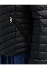 Zwarte pufferjas met geborduurd patroon, met een ritszak aan de zijkant. Glad materiaal, slanke pasvorm en minimalistische ontwerpelementen.