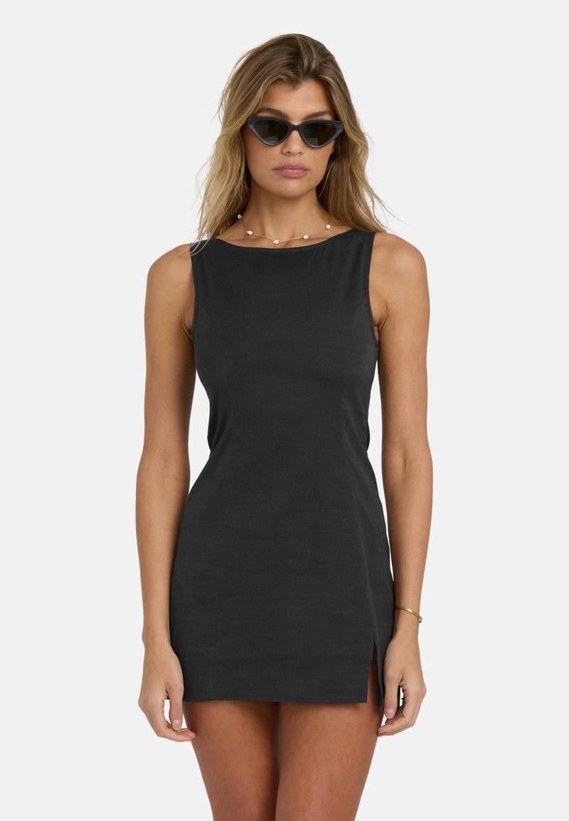 Woman wearing black sleeveless mini dress with side slit, cat-eye sunglasses, a shell necklace, and a gold bracelet on her right wrist.
