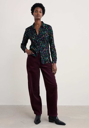 Zwarte button-up shirt met bloemenpatroon, gecombineerd met bordeaux brede corduroy broek en zwarte enkelboots, met textuurdetails in de stof.