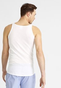 Débardeur en coton blanc avec des bretelles étroites, design légèrement ajusté et texture lisse. Vue de dos, complété par un short bleu clair.