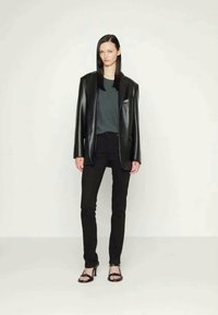 Črn usnjen blazer, oblečen čez temno sivo majico, v kombinaciji s črnimi skinny jeans in z visokimi sandali s trakci. Preprost, natančno krojen dizajn.