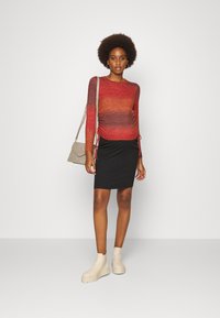 Blusa de manga longa em degradê vermelho, com lados franzidos, combinada com uma saia preta em malha e botas de cano curto bege. Acessórios incluem uma mala cinza.