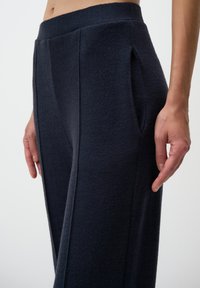 Marineblauwe broek van een gestructureerde stof, met zijzakken en subtiele plooien, ontworpen met een hoge tailleband voor een getailleerde pasvorm.