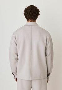 Light gray oversized jacket with a collar, clean lines, and long sleeves. Smooth texture with buttoned cuffs and minimal detailing.
