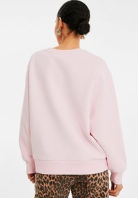 Helles rosa Sweatshirt mit gerippten Bündchen und Saum, ausgestattet mit einer lockeren Passform; getragen mit braunen Hose im Leopardenmuster. Weiches Baumwollmischgewebe.