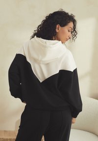 Das Kapuzen-Sweatshirt verfügt über ein Color-Block-Design in Weiß und Schwarz. Der Stoff wirkt weich, mit einem lockeren Schnitt und gerippten Bündchen.