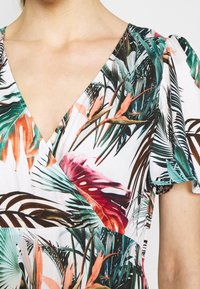 Blommig klänning med V-ringning, korta puffärmar och en blandning av gröna, rosa och orange botaniska mönster på vit bakgrund.