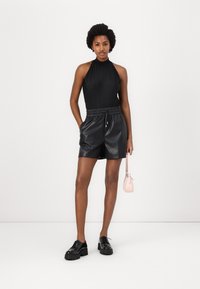 Black pleated halter bodysuit paired with high-waisted black leather shorts and black platform shoes, holding a small pink handbag.