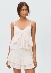 White layered top and skirt set made from lightweight fabric. Features adjustable straps, ruffled tiers, and scalloped edges.
