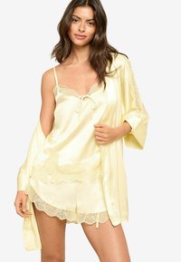 Costum de somn din satin galben, cu detalii din dantelă. Include un maieu cu bretele subțiri și pantaloni scurți, stratificat cu un halat asortat în stil kimono.
