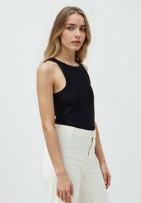 Top senza maniche nero realizzato in tessuto liscio, con scollatura rotonda e vestibilità leggermente ampia, abbinato a pantaloni bianchi a vita alta.