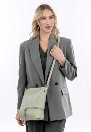 Light green leather bag with a zippered pocket, rectangular shape, adjustable strap, and a smooth texture, held by a person in a gray blazer.