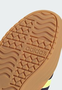 Zool van een Adidas-schoen in lichtbruin rubber met driehoekige en golvende profielpatronen, met het Adidas-logo in het midden.