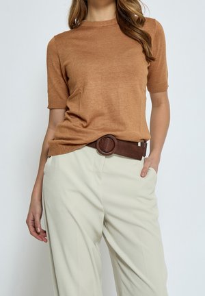 Mujer con un top marrón de punto de manga corta metido en pantalones beige de cintura alta con un cinturón texturizado marrón oscuro.