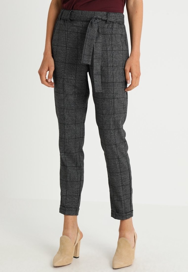 Pantalons à carreaux gris avec une ceinture, coupe ajustée et texture lisse. Portés avec des mules nude, présentant un design à dos ouvert.