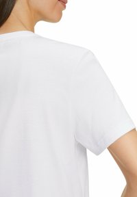 T-shirt in cotone bianco con maniche corte. Tessuto liscio con scollatura a girocollo e orlo cucito. Presenta una vestibilità rilassata e un design minimalista.