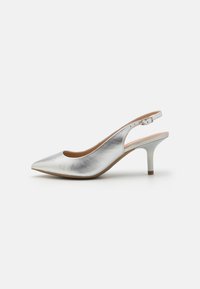 Srebrni metalni slingback pump, koničast nos, tanek pet, gladka tekstura in nastavljiv trak okoli gležnja z diskretno rjavim poudarkom na podplatu.