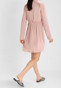 Ljusrosa långärmad klänning med elastisk midja och spetsdetaljer på axlarna. Bärs med svart och vit randig slip-in sandal.