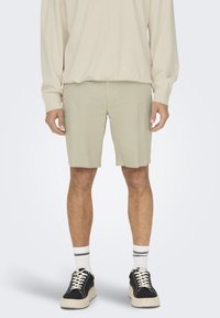 Lysgrønne shorts lavet af et blødt stof, knælange med en glat tekstur, parret med sorte sneakers og hvide, stribede sokker.