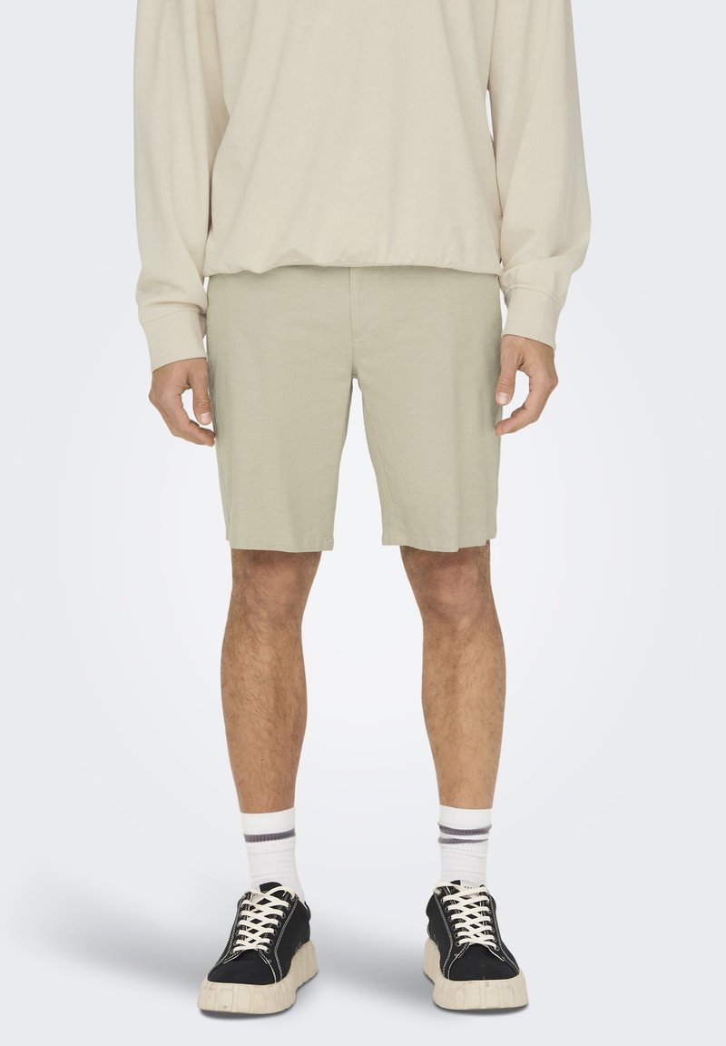 Lysgrønne shorts lavet af et blødt stof, knælange med en glat tekstur, parret med sorte sneakers og hvide, stribede sokker.