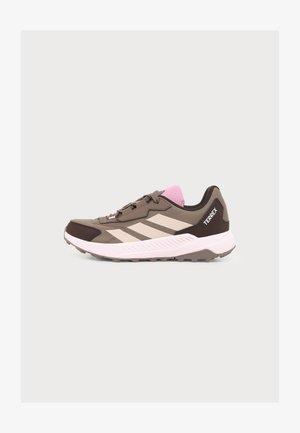 Bruine en beige Adidas Terrex sneaker met roze tong, witte zool en drie beige strepen aan de zijkant, in profiel weergegeven op een witte achtergrond.