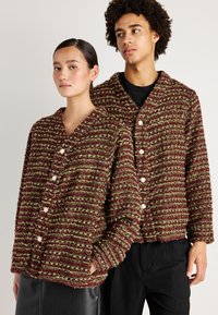 Červené a zelené pruhované textúrované cardiganové svetre s voľným strihom, s V-výstrihom a bielymi gombíkmi, ktoré sú na sebe oblečené dvoma osobami.