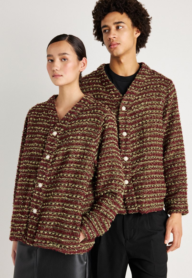 Červené a zelené pruhované textúrované cardiganové svetre s voľným strihom, s V-výstrihom a bielymi gombíkmi, ktoré sú na sebe oblečené dvoma osobami.