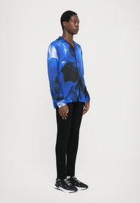 Camicia blue a fantasia con maniche lunghe e chiusura con bottone, abbinata a pantaloni neri slim-fit e sneakers nere.
