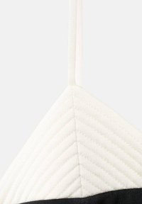 Bralette triangle avec un tissu blanc doux et matelassé en haut et une base noire contrastante. Les bretelles sont fines et texturées.