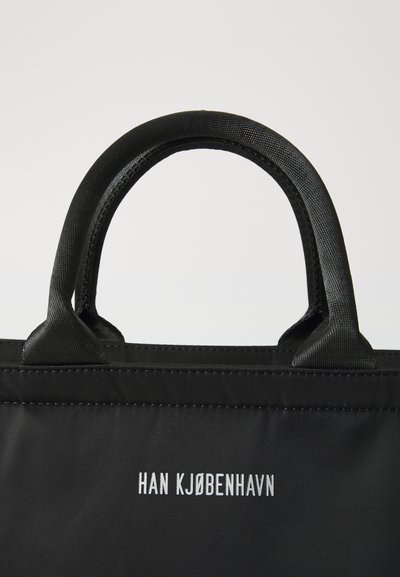Black tote bag with sturdy fabric, short handles, and white branding text "HAN KJØBENHAVN" on the front. Simple and functional design.