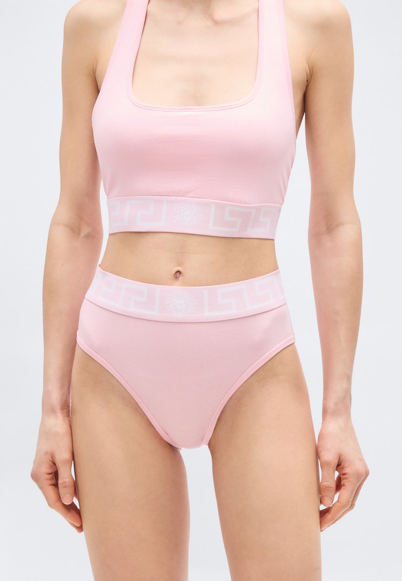Γυναίκα που φοράει σετ εσωρούχων μ ε ψηλή μέση και τοπ σε ανοιχτό ροζ χρώμα, με μοτίβα στα ελαστικά λάστιχα και λεπτομέρειες με το λογότυπο Medusa.
