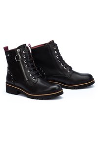 Stivali alla caviglia in pelle nera con punta rotonda, lacci frontali, zip laterale e borchie decorative sul tallone. Suola in gomma con un leggero tacco.