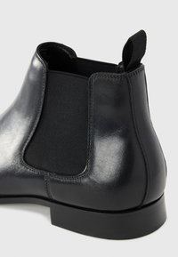 Botín Chelsea de cuero negro con acabado suave, paneles laterales elásticos y una lengüeta. La suela es plana y está hecha de goma.