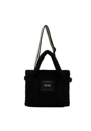 Borsa tote in finta pelliccia nera con manici corti e una tracolla rimovibile a righe. Presenta una patch logo rettangolare sul davanti.
