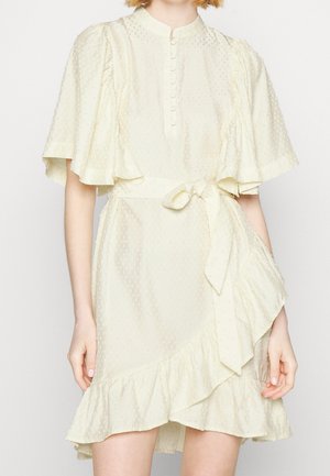 Cream textured short dress with flutter sleeves, buttoned front, ruffled hem, and a tied waist belt on a standing woman.
