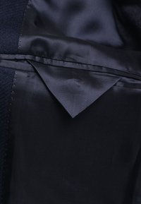 Ciemnogranatowa podszewka z satyny w kurtce z widoczną klapką kieszeni i starannym przeszyciem wzdłuż szwu.