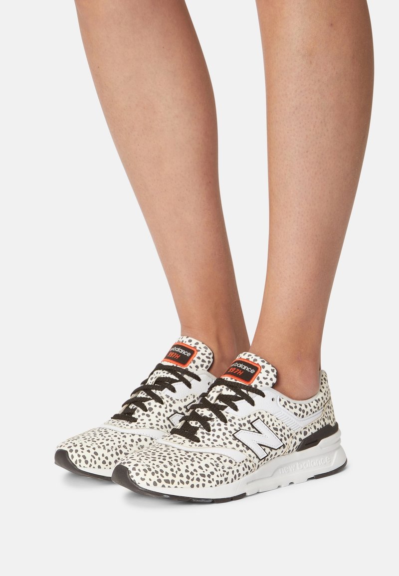 Baskets blanches avec des éclaboussures noires, tige en maille et synthétique, lacets noirs, étiquettes oranges et semelle intermédiaire moulée. Le design présente un bout rond.