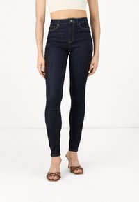 Jeans de tiro alto de color azul oscuro, hechos de denim, con un corte slim, diseño clásico de cinco bolsillos y detalles de costura en contraste.